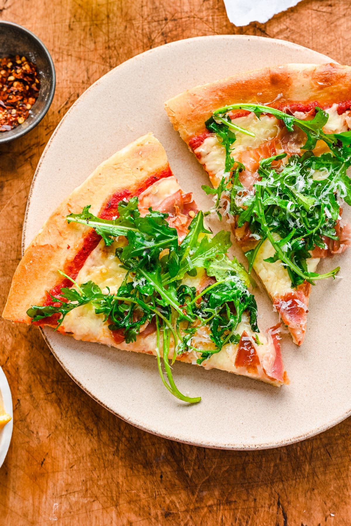Two slices of arugula prosciutto pizza on a white plate.