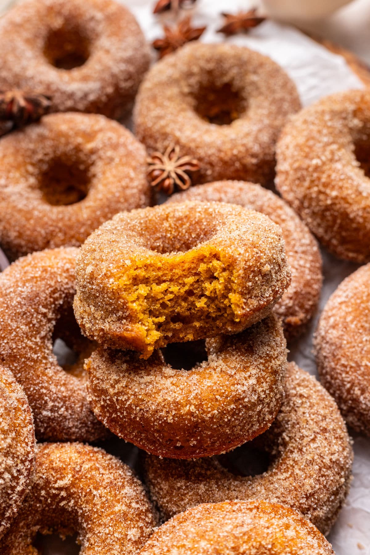 A baked pumpkin with a bite missing on top of overlapping baked pumpkin donuts.