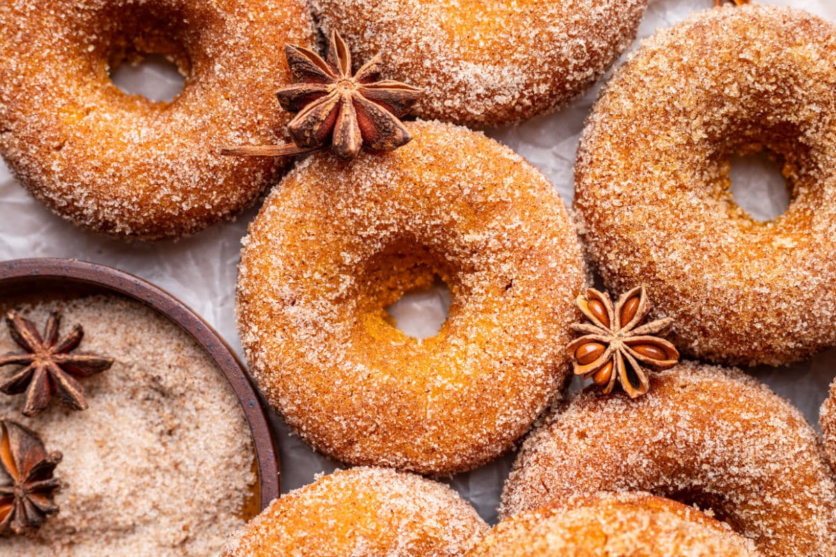 Star anise and a dish of cinnamon sugar next to baked pumpkin donuts.