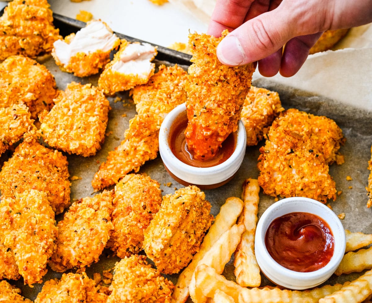 A hand dipping a baked nugget in sauce.