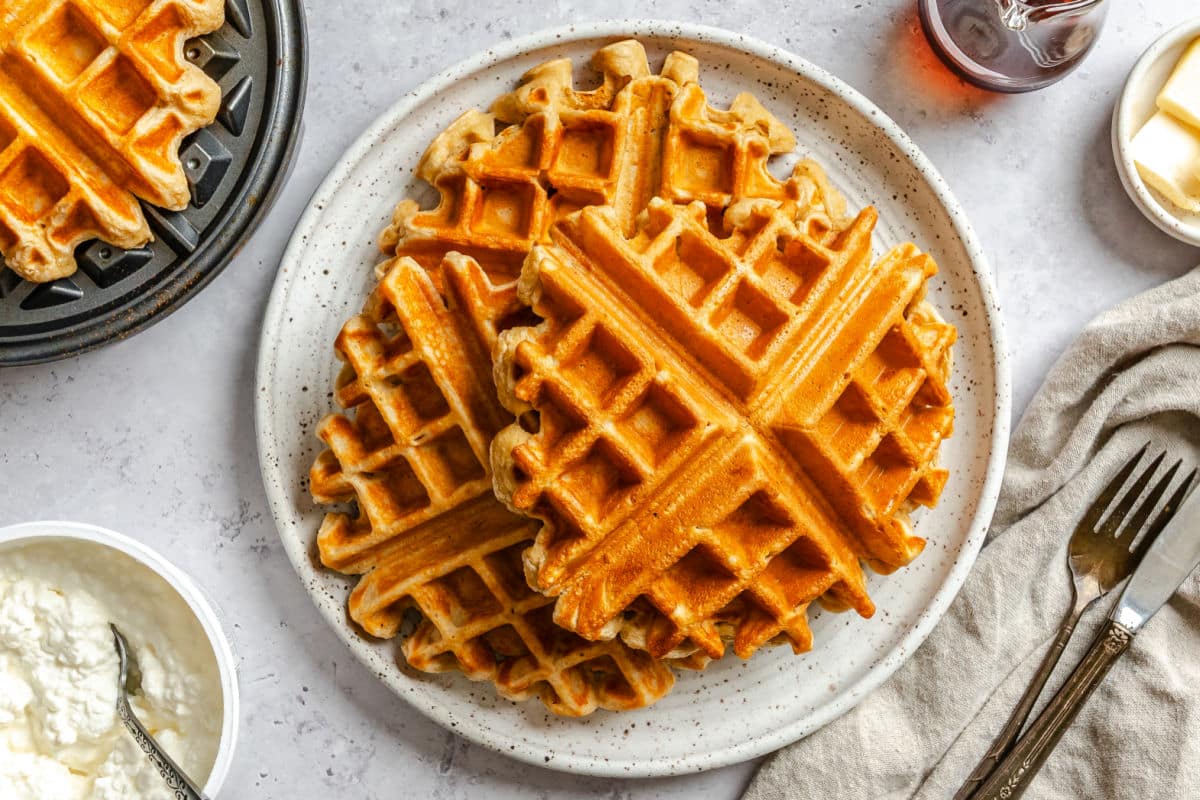 Three cottage cheese waffles on a plate next to the waffle iron.