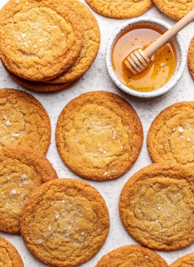 Overlapping honey cookies next to a dish of honey with a honey dipper in it.