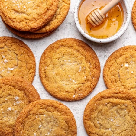 Overlapping honey cookies next to a dish of honey with a honey dipper in it.
