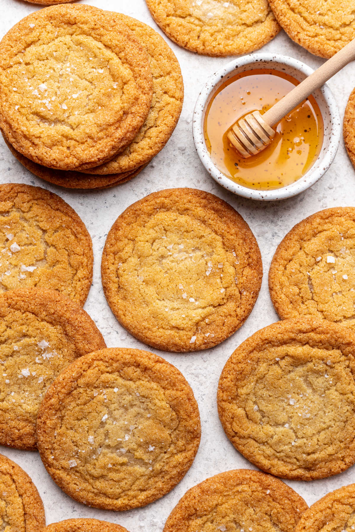 Overlapping honey cookies next to a dish of honey with a honey dipper in it.