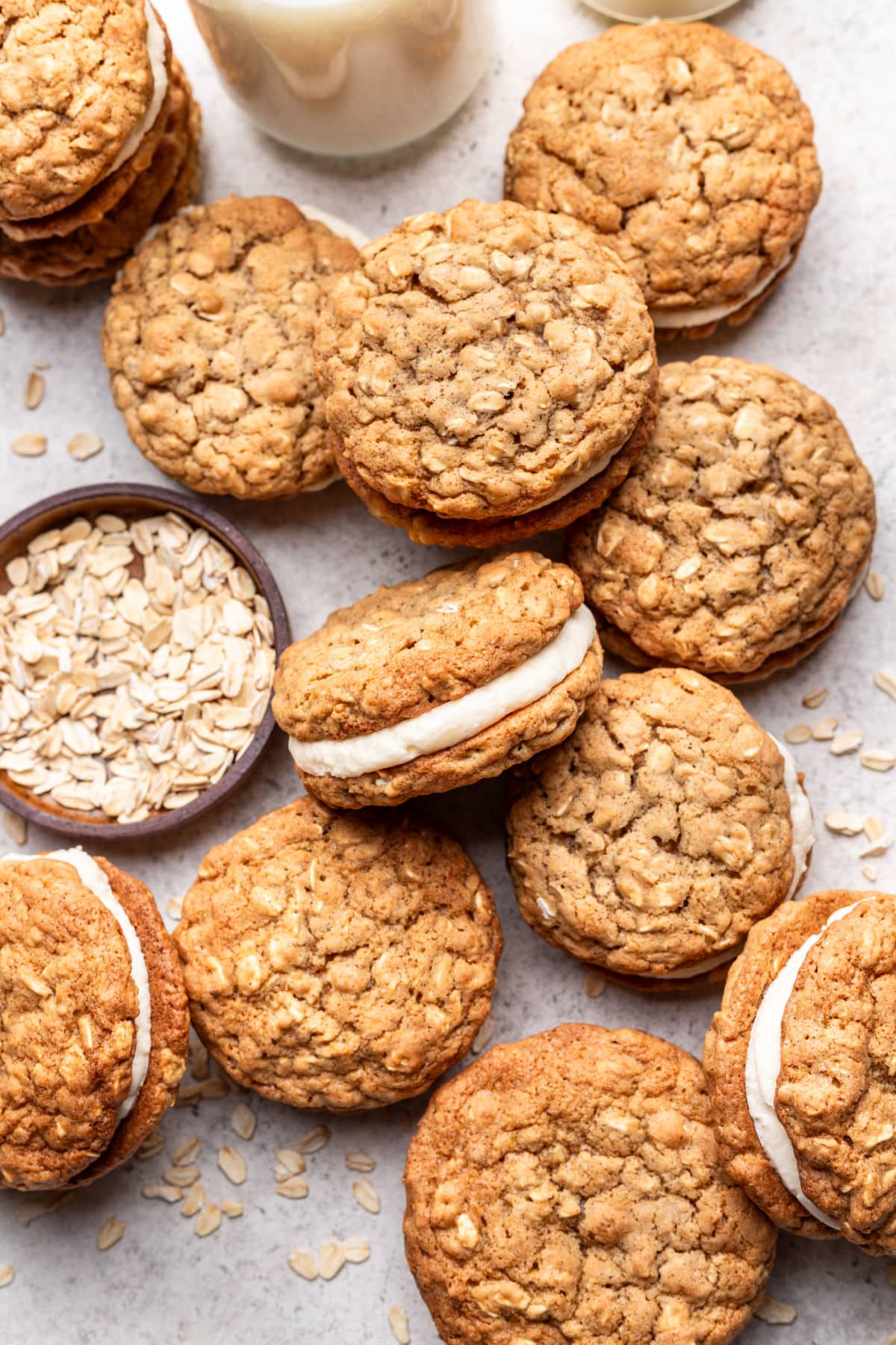 Oatmeal cream pies next to a glass of milk and a dish of oats.