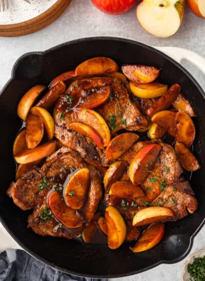 A skillet of pork chops and apples next to stacked plates.