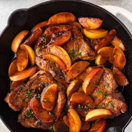 A skillet of pork chops and apples next to stacked plates.