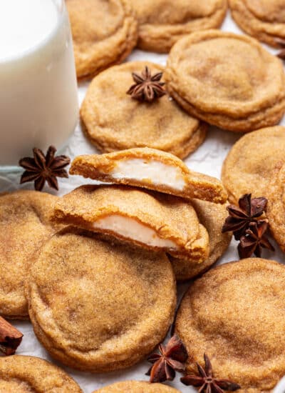 A pumpkin cheesecake cookie broken in half next to more overlapping cookies.