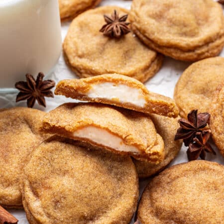 A pumpkin cheesecake cookie broken in half next to more overlapping cookies.