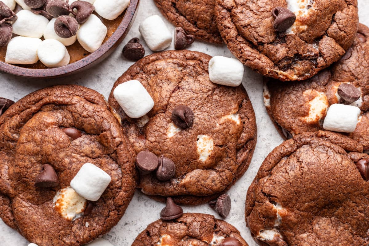 Chocolate marshmallow cookies next to a dish of marshmallows and chocolate chips.