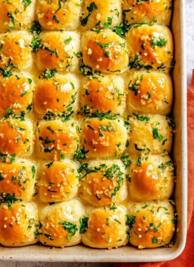Garlic butter rolls in a baking pan next to an orange kitchen towel.