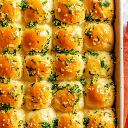 Garlic butter rolls in a baking pan next to an orange kitchen towel.