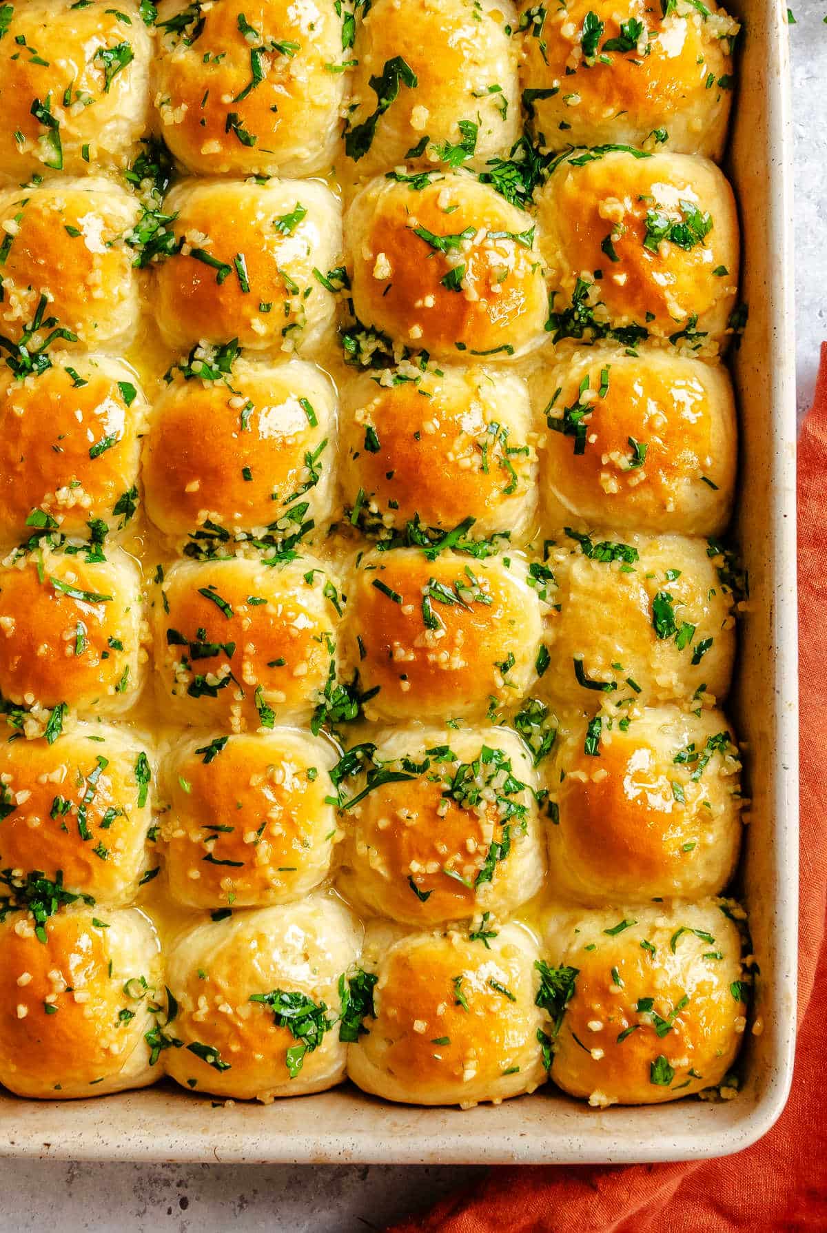 Garlic butter rolls in a baking pan next to an orange kitchen towel.