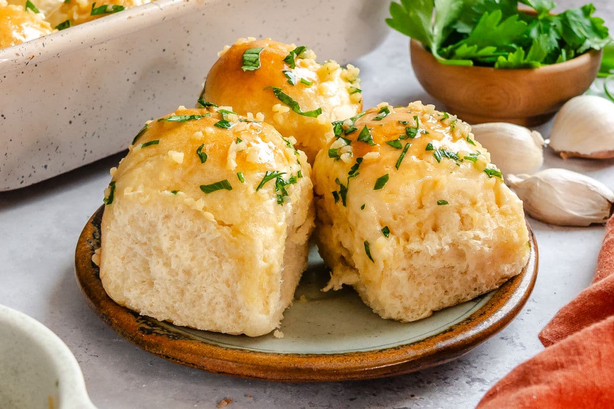 Three garlic butter rolls on a plate next to a dish of parsley.