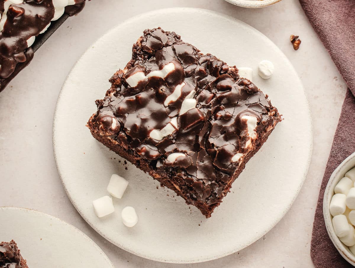 A piece of Mississippi mud cake on a plate with marshmallows next to it.
