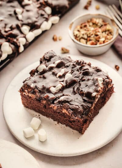 A slice of Mississippi mud cake on a plate next to a dish of nuts.