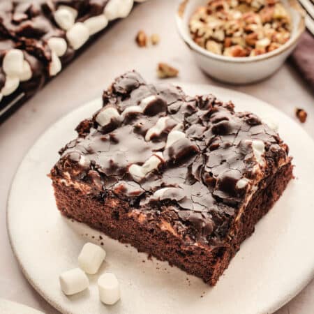 A slice of Mississippi mud cake on a plate next to a dish of nuts.