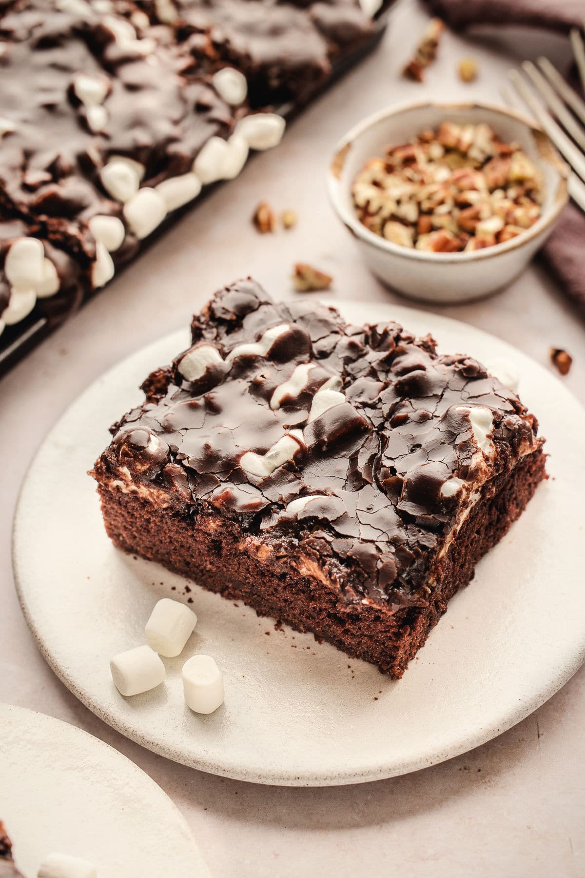 A slice of Mississippi mud cake on a plate next to a dish of nuts.