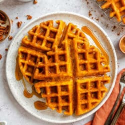 Two pumpkin waffles on a plate next to a mug of coffee.