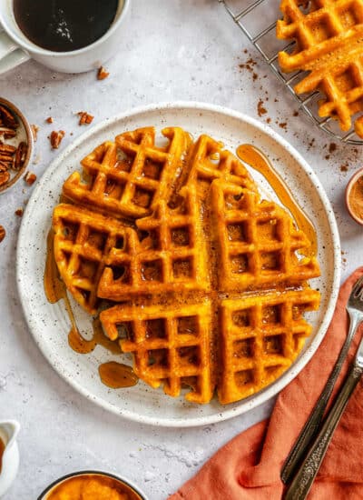 Two pumpkin waffles on a plate next to a mug of coffee.