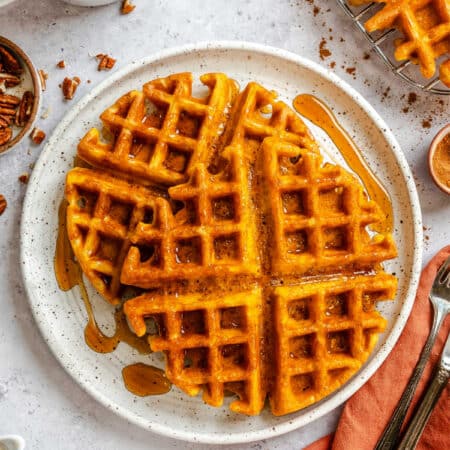 Two pumpkin waffles on a plate next to a mug of coffee.