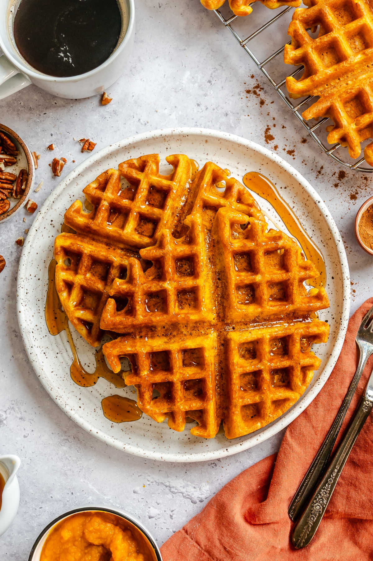 Two pumpkin waffles on a plate next to a mug of coffee.