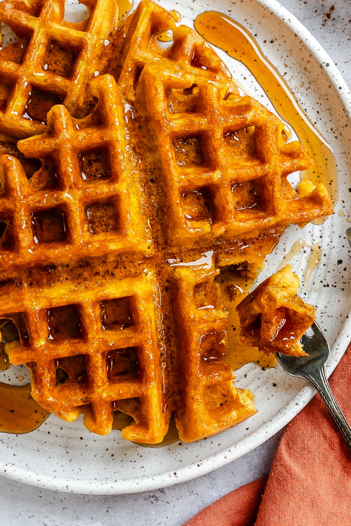 A fork taking a bite from a plate of pumpkin waffles.