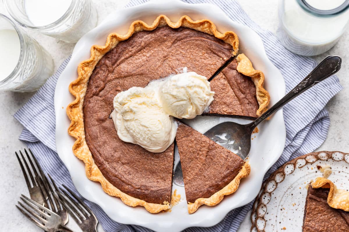 A partially sliced brownie pie topped with two scoops of vanilla ice cream.