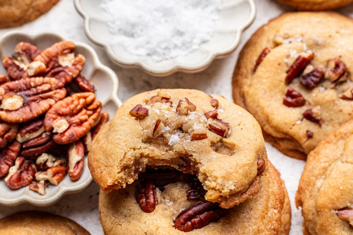 A butter pecan cookie with a bite missing on top of other cookies. 