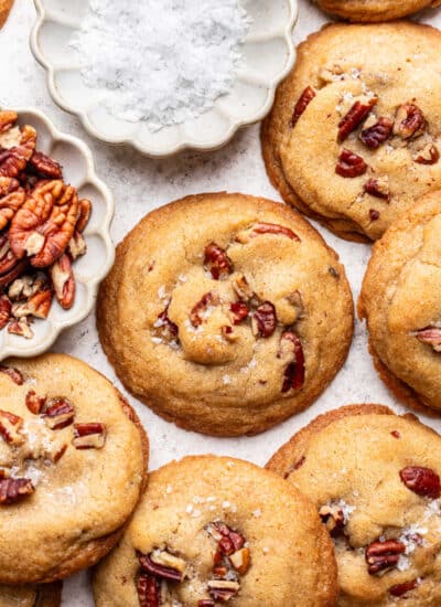 Butter pecan cookies overlapping next to a dish of salt.
