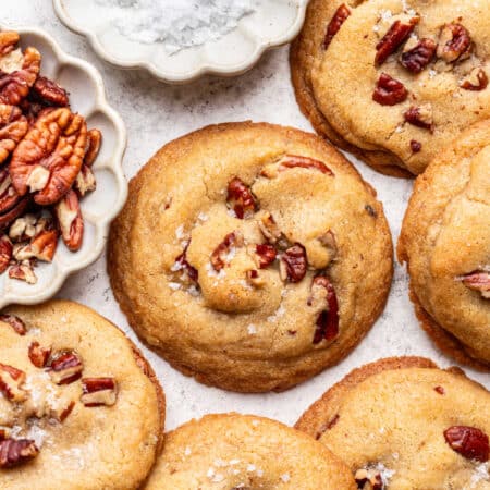 Butter pecan cookies overlapping next to a dish of salt.
