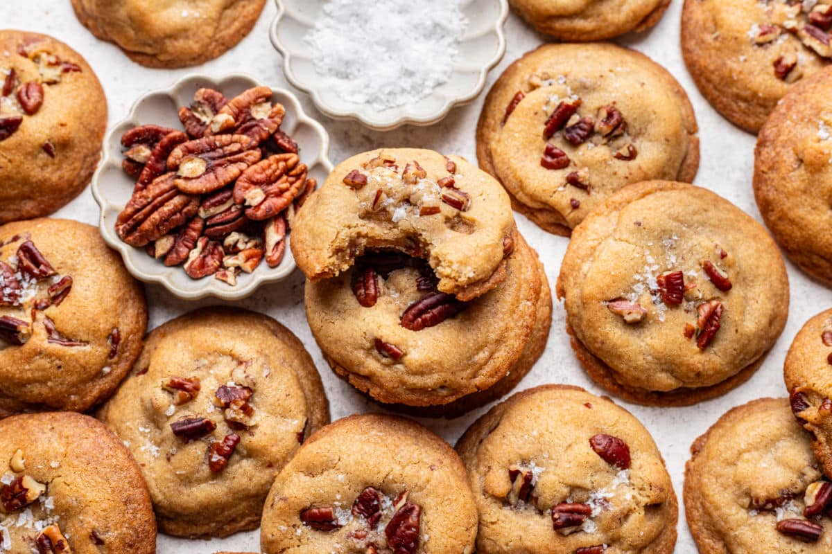 Butter pecan cookies next to a dish of chopped pecans and a dish of salt. 