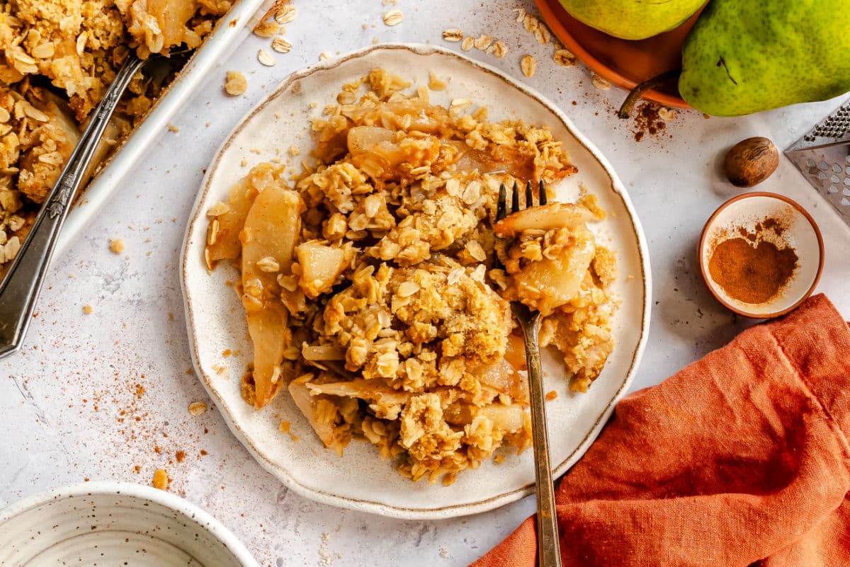 A plate of pear crisp next to the pan of crisp. 