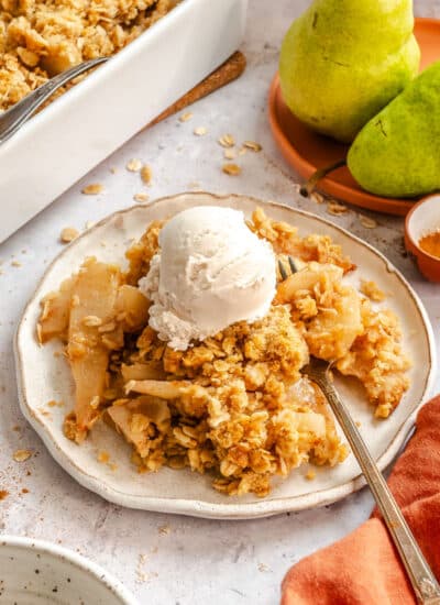 Plate of pear crisp topped with a scoop of vanilla ice cream.