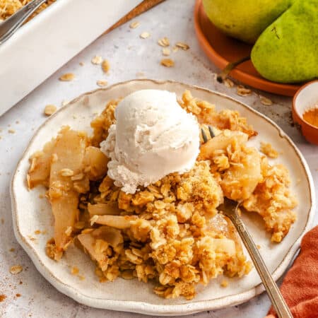 Plate of pear crisp topped with a scoop of vanilla ice cream.