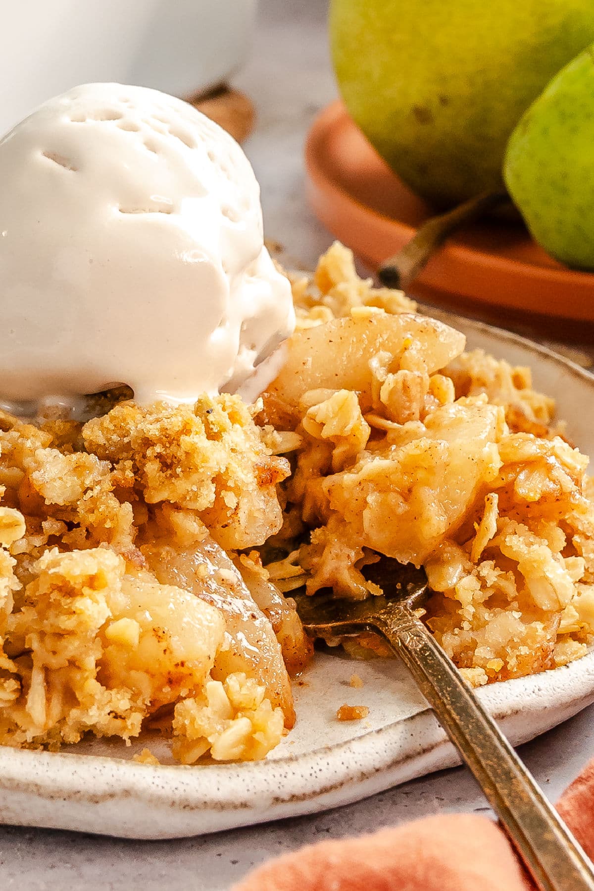 A plate of pear crisp topped with vanilla ice cream with a fork taking a bite out of it.